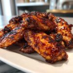 A close-up of a pile of glistening BBQ Air Fryer Wings on a white plate, showing their crispy texture and rich glaze.