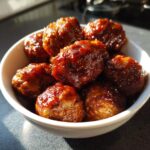 A close-up shot of a white bowl filled with glistening, saucy BBQ meatballs.