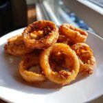 A pile of golden-brown, crispy beer-battered onion rings on a white plate, ready to be enjoyed.