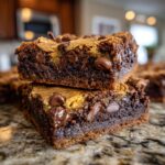 Close-up of two fudgy chewy brookies stacked on a granite countertop, loaded with chocolate chips.