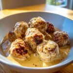 Close-up of Classic Swedish Meatballs bathing in a rich, creamy sauce in a white bowl.