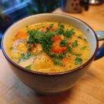 A close-up of a steaming bowl of Cozy One-Pot Creamy Vegetable Soup, filled with chunks of carrots, potatoes, and herbs.