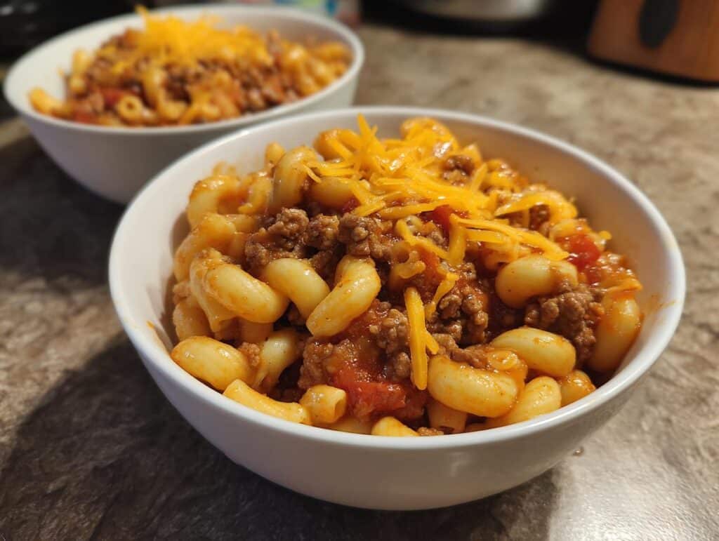 Close-up of a bowl of Easy Classic Goulash Recipe with Ground Beef and Macaroni topped with shredded cheese.