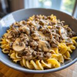 A close-up of a bowl filled with Easy Hamburger Stroganoff served over fluffy egg noodles, featuring ground beef and mushrooms in a creamy sauce.
