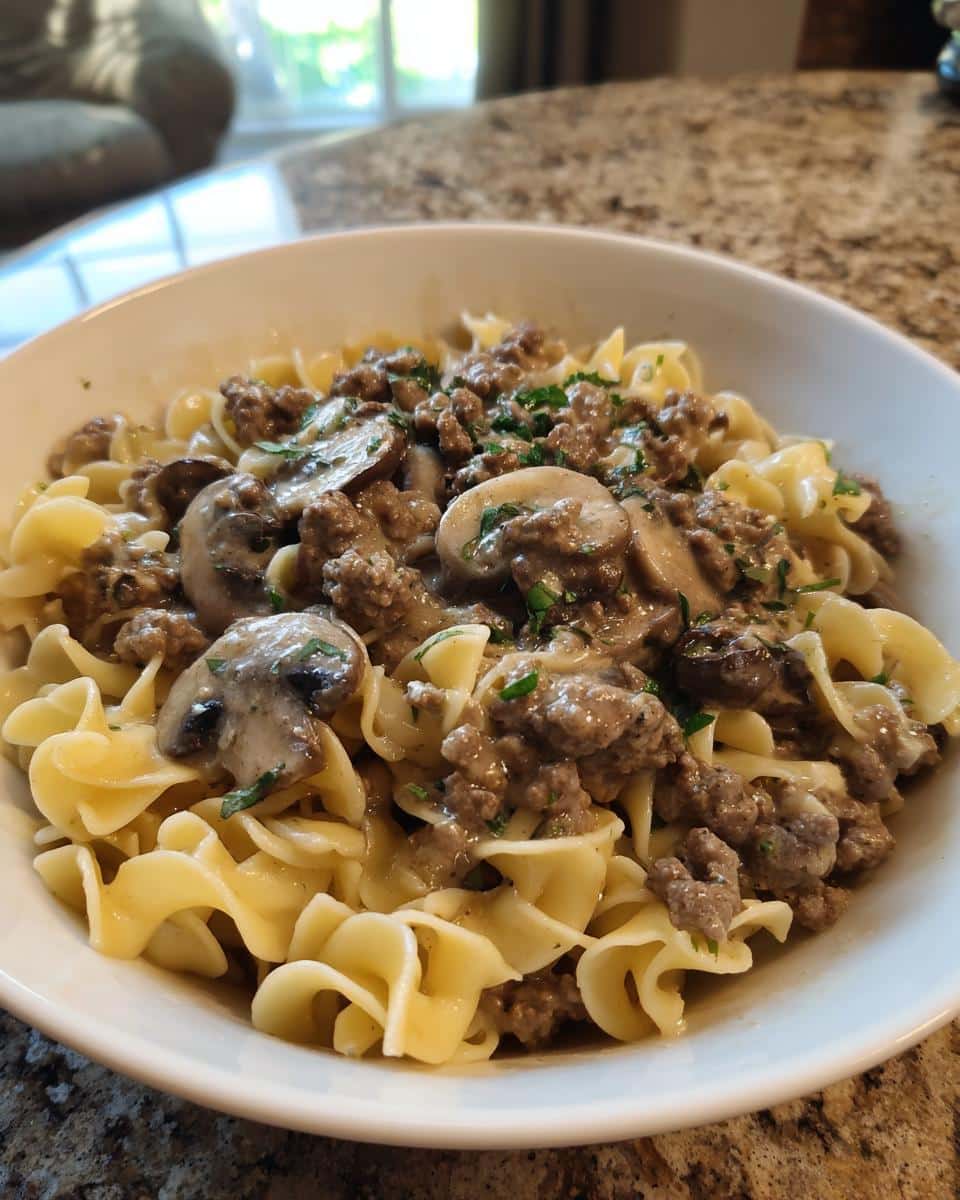 A bowl of Easy Hamburger Stroganoff with Egg Noodles, featuring ground beef, mushrooms, and a creamy sauce, garnished with parsley.