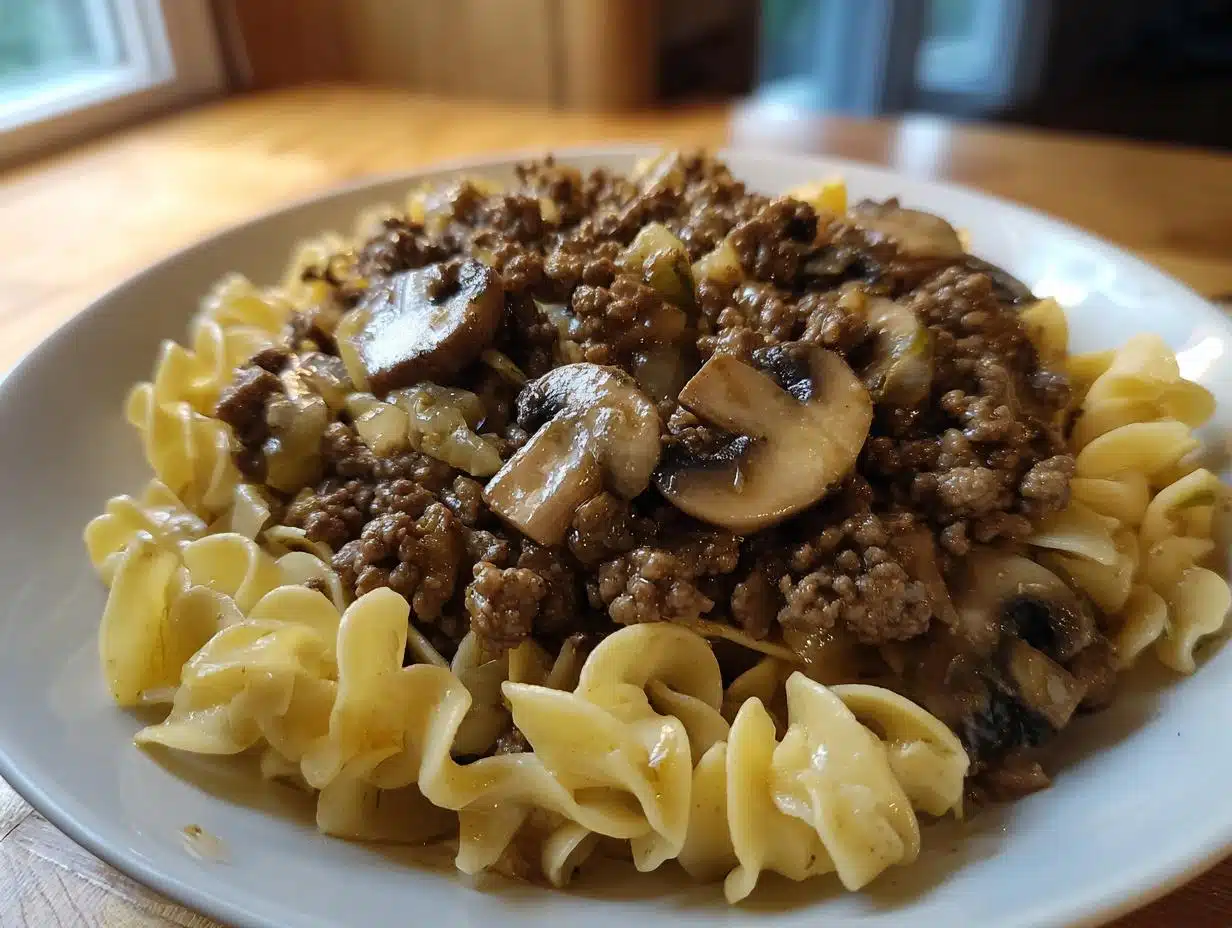 A close-up of a white plate filled with Easy Hamburger Stroganoff served over wide egg noodles, featuring ground beef and mushrooms.