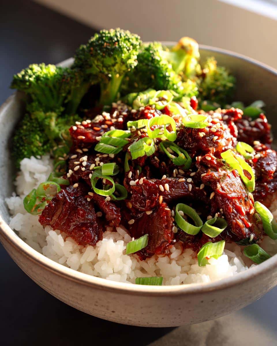 A close-up of an Easy Korean Gochujang Beef Bowl with white rice, tender gochujang beef, steamed broccoli, and garnished with sesame seeds and green onions.