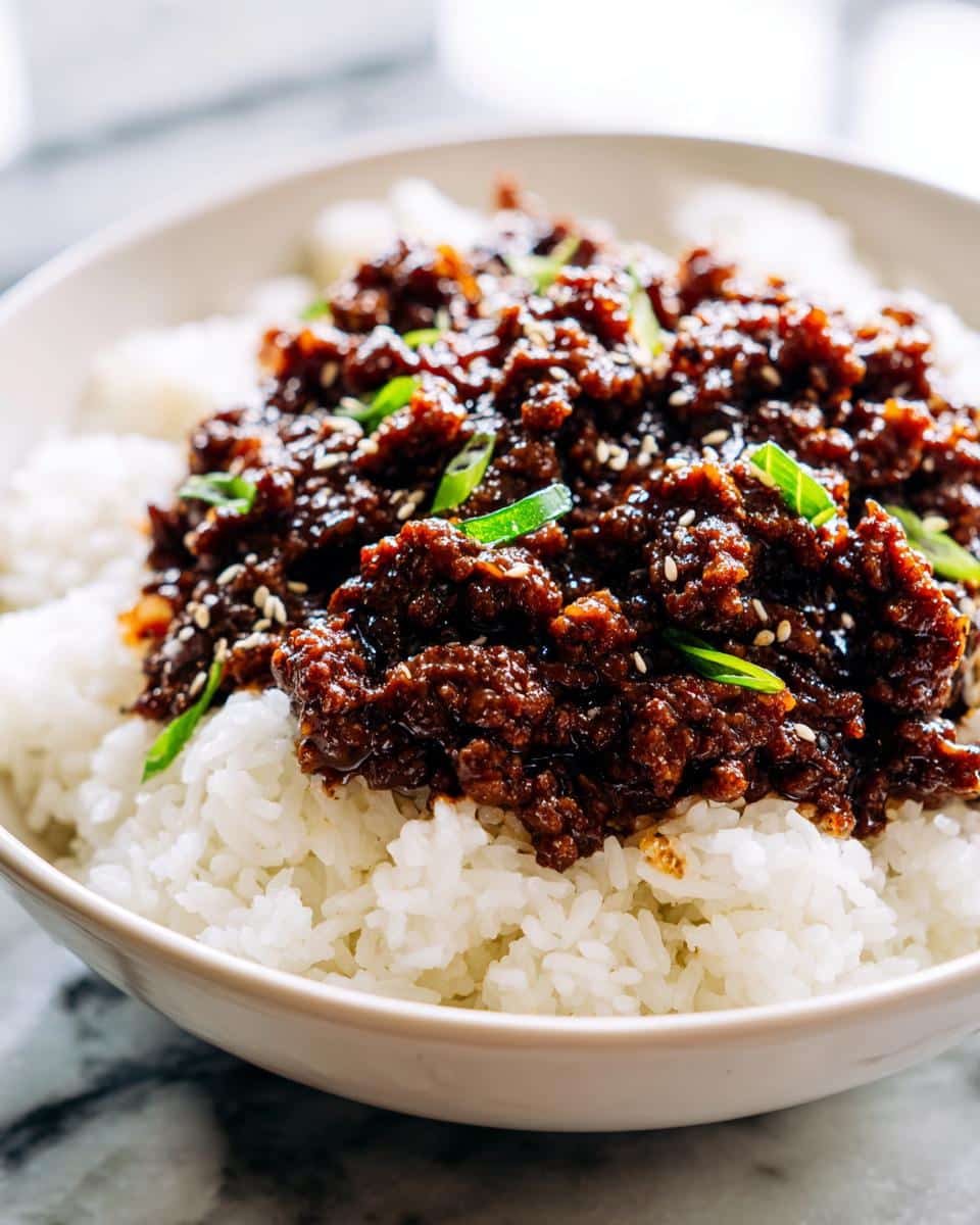 Close-up of a bowl of white rice topped with savory Mongolian ground beef and garnished with green onions and sesame seeds.