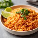 A close-up bowl of fluffy Easy Restaurant Style Mexican Rice, garnished with cilantro and lime wedges.