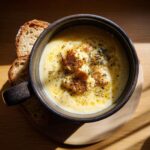 A bowl of creamy Easy Roasted Cauliflower Soup topped with roasted cauliflower florets and herbs, served with toasted bread.
