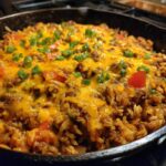Close-up of a skillet filled with cheesy ground beef and rice, topped with chopped green onions.