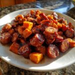 A close-up shot of a white plate filled with glistening Honey Garlic Sausage Sweet Potatoes, showcasing caramelized chunks.