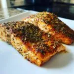 Close-up of two perfectly cooked Spicy Cajun Air Fryer Salmon fillets seasoned with herbs.