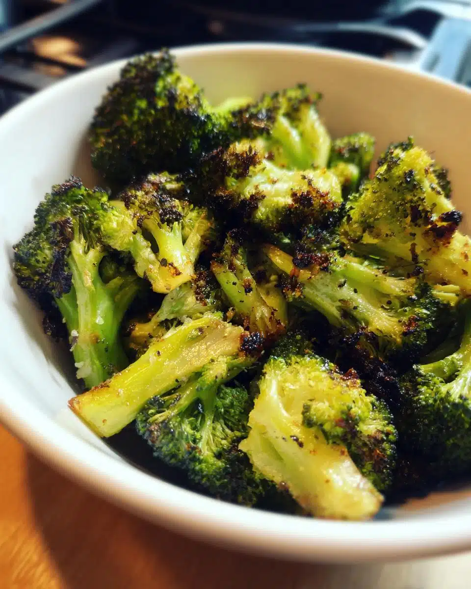Close-up of perfectly crispy air fryer broccoli florets in a white bowl, seasoned and slightly charred.