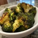 Close-up of perfectly crispy air fryer broccoli florets seasoned and served in a white bowl.