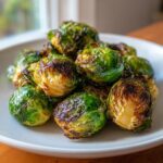 A pile of perfectly crispy air fryer brussels sprouts on a white plate, showing their charred edges and vibrant green color.