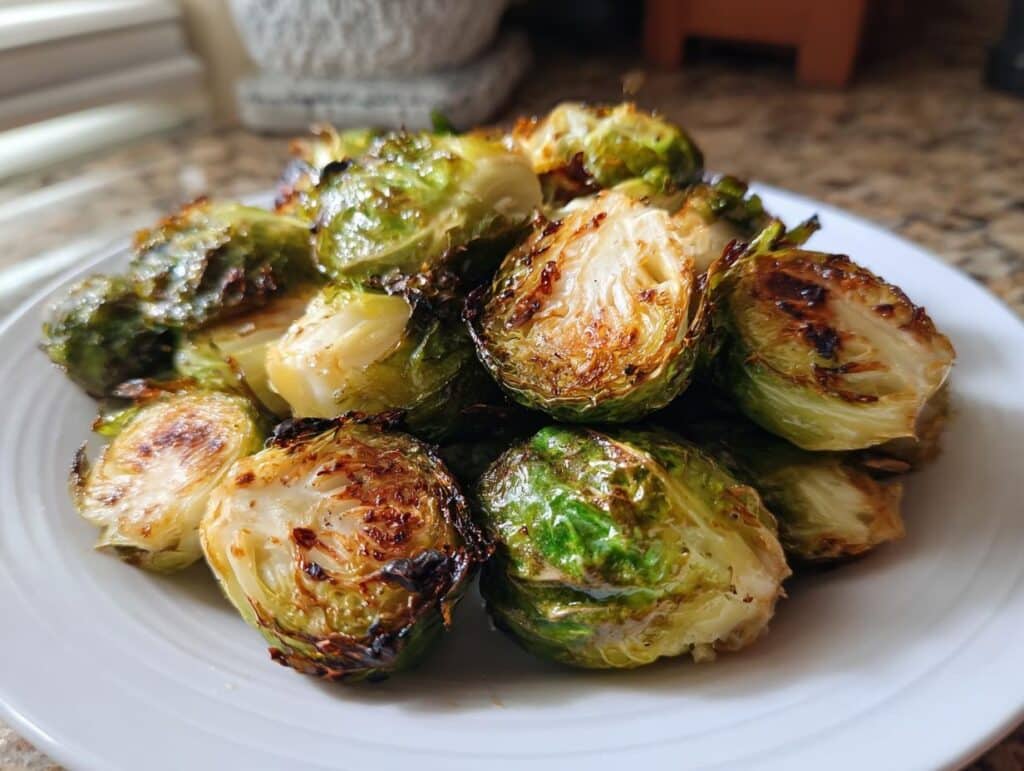 A white plate filled with perfectly cooked air fryer brussels sprouts, some halved to show their tender interior and crispy edges.