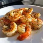 A close-up of perfectly cooked air fryer shrimp seasoned with herbs and spices on a white plate.