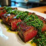 Close-up of perfectly cooked air fryer steak slices topped with vibrant chimichurri sauce.