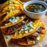 Close-up of authentic Birria Tacos filled with shredded beef, topped with diced onions and cilantro, served with a side of consomé.