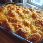 A freshly baked chicken crescent roll casserole with melted cheddar cheese topping in a glass baking dish.