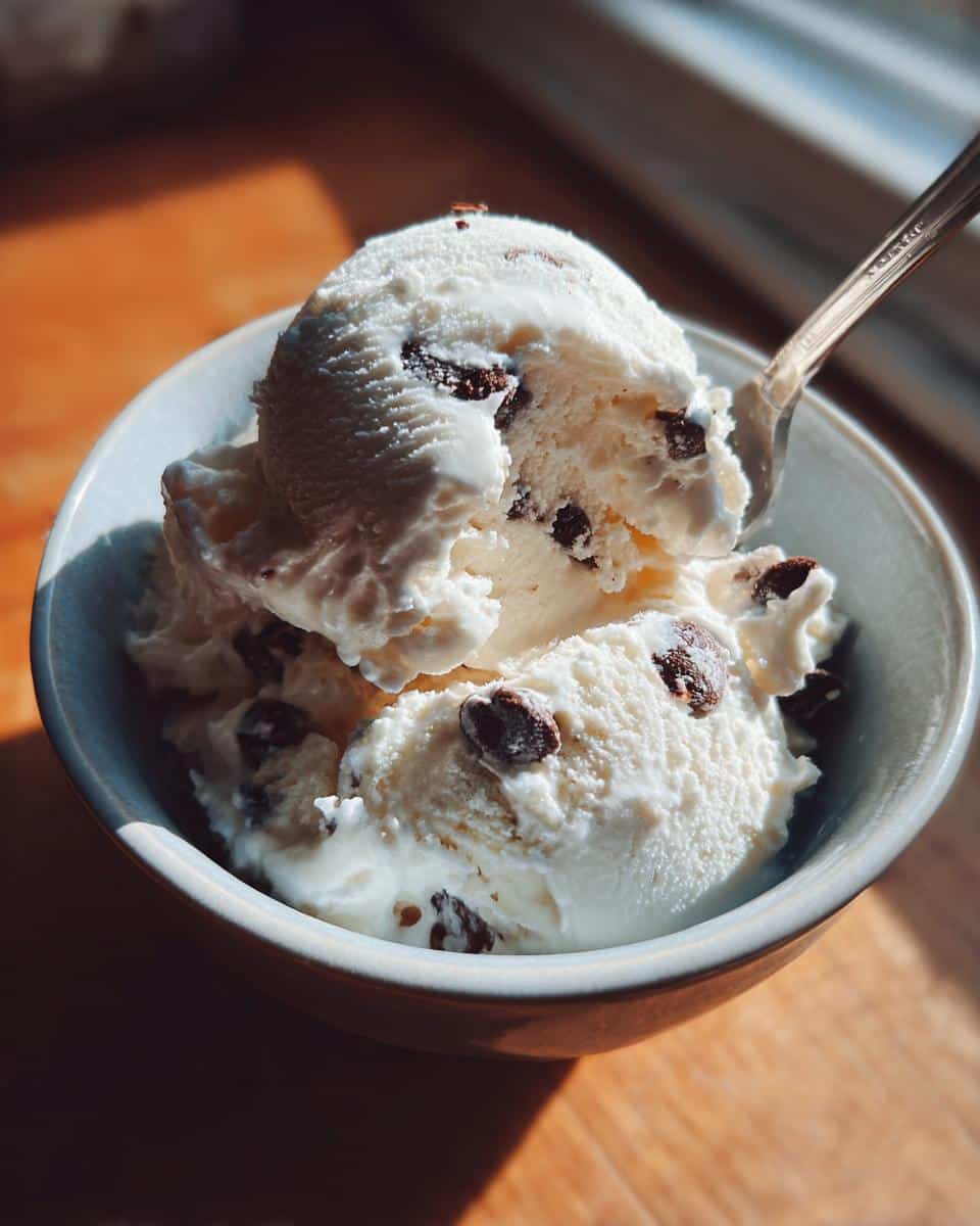A bowl filled with scoops of creamy cottage cheese ice cream studded with chocolate chips, with a spoon taking a bite.