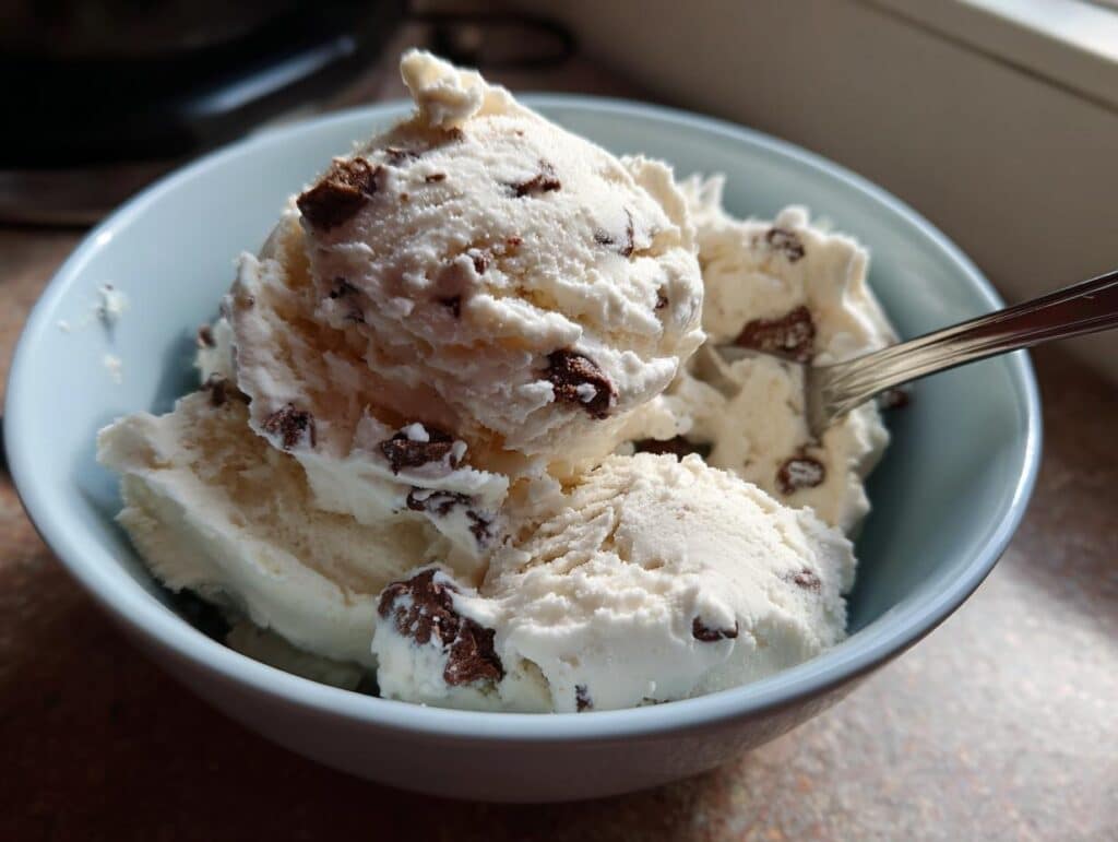 A light blue bowl filled with creamy cottage cheese ice cream loaded with dark chocolate chunks.