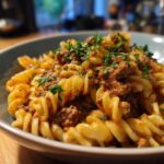A bowl of creamy goulash with ground beef and fusilli pasta, topped with fresh parsley.