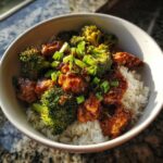 A delicious bowl of crockpot chicken and broccoli served over white rice, garnished with green onions.