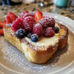 A slice of Custard Yogurt Toast topped with creamy custard, fresh raspberries, blueberries, and strawberries, dusted with powdered sugar.