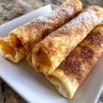 Close-up of three sweet dessert tortilla wraps dusted with cinnamon sugar and powdered sugar on a white plate.