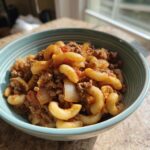 A close-up of a bowl filled with easy goulash recipe ground beef and macaroni pasta, with visible chunks of onion and tomato sauce.