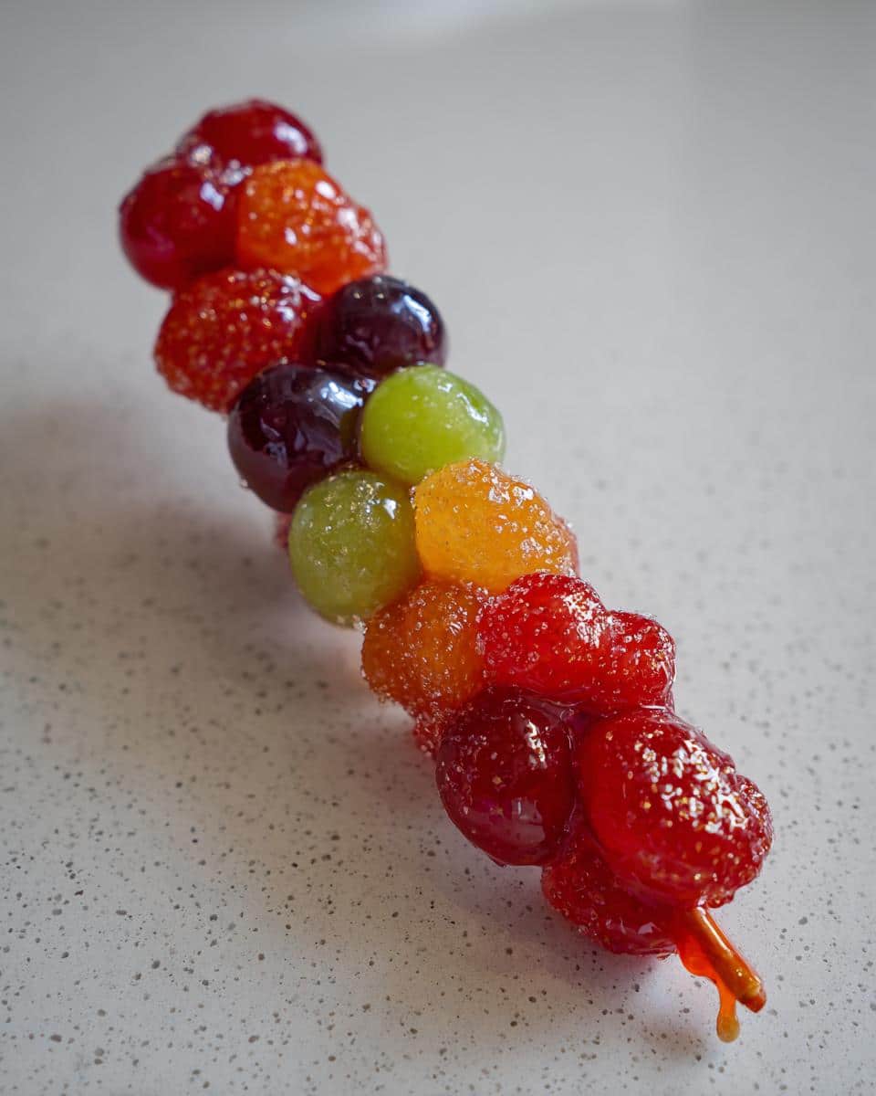 Close-up of an Easy Tanghulu Recipe skewer with colorful candied grapes and berries.