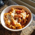 Close-up of a white bowl filled with a cheesy pasta bake, a perfect example of family friendly pasta recipes.