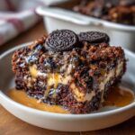 A decadent slice of Fast Oreo Dump Cake Recipe, topped with Oreos and drizzled with caramel sauce.