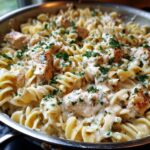 A close-up of a skillet filled with gluten free garlic butter chicken pasta, garnished with fresh parsley.