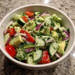 A close-up of a vibrant Green Goddess Chop Salad in a white bowl, featuring chopped avocado, cucumber, tomatoes, and red onion.