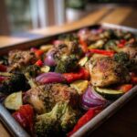 A close-up of a sheet pan filled with roasted chicken thighs, broccoli, red onion, bell peppers, and zucchini, perfect for healthy family dinner ideas.