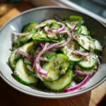 Close-up of Logan's Cucumber Salad featuring thinly sliced cucumbers, red onion rings, and fresh dill in a grey bowl.