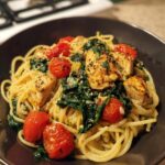 A close-up of a bowl of low calorie chicken pasta, featuring tender chicken pieces, cherry tomatoes, and wilted spinach.