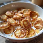 A close-up shot of a bowl filled with Mini Pancake Cereal swimming in milk, drizzled with syrup.