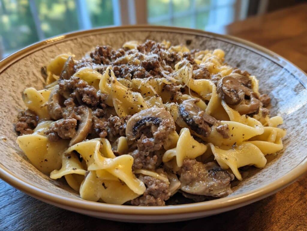 A hearty bowl of one pot hamburger stroganoff with egg noodles, mushrooms, and ground beef, topped with grated cheese.
