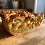 A slice of golden-brown Pizza Pot Pie featuring pasta, cheese, and tomato filling on a wooden board.