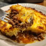 A fork lifts a generous portion of Shepherd's Pie, revealing layers of savory ground meat and creamy mashed potatoes, a perfect comfort food recipe.