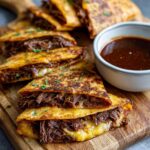 Close-up of crispy slow cooker birria tacos filled with shredded beef and melted cheese, served with a side of consommé.