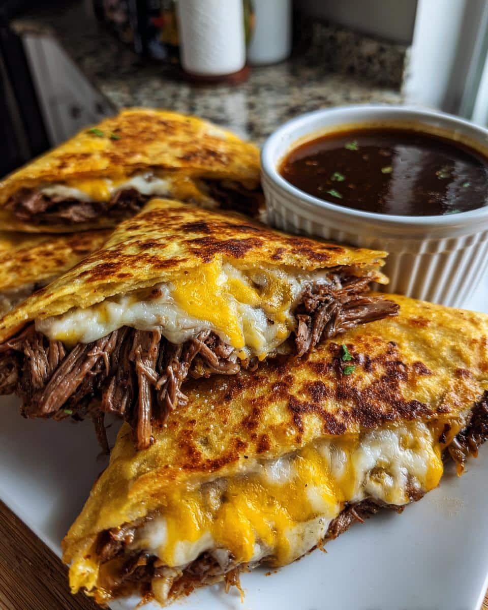 Close-up of cheesy slow cooker birria tacos served with a side of rich consommé for dipping.
