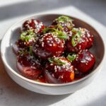 A bowl of glossy, dark red spicy boiled eggs, garnished with sesame seeds and green onions.