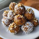 A pile of round vegan no bake pumpkin bites rolled in shredded coconut and topped with chopped nuts.