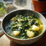A steaming bowl of vegetarian caldo verde soup with potatoes and kale, served in a rustic bowl.