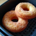 Two golden Air Fryer Donuts coated in sugar, sitting in the air fryer basket.